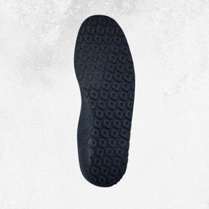 A top-down view of a black shoe sole with a detailed geometric tread pattern, set against a light gray textured background.