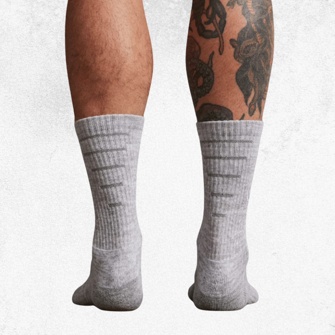 A pair of light gray ribbed crew socks worn on a person's legs, shown from the back against a light gray textured background.