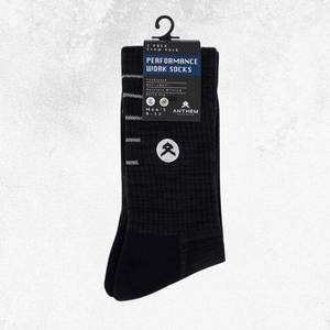 A pair of black performance work socks hanging from a black plastic hanger with a product label. The socks feature a subtle grid pattern and a white circular logo on the lower leg.