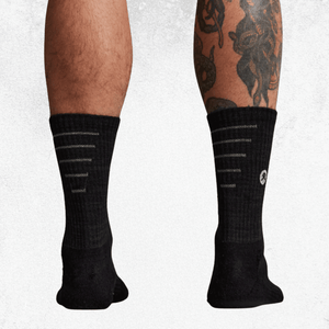 Black crew socks with white horizontal stripe details and a small circular logo, shown worn on a person's legs against a light gray background.