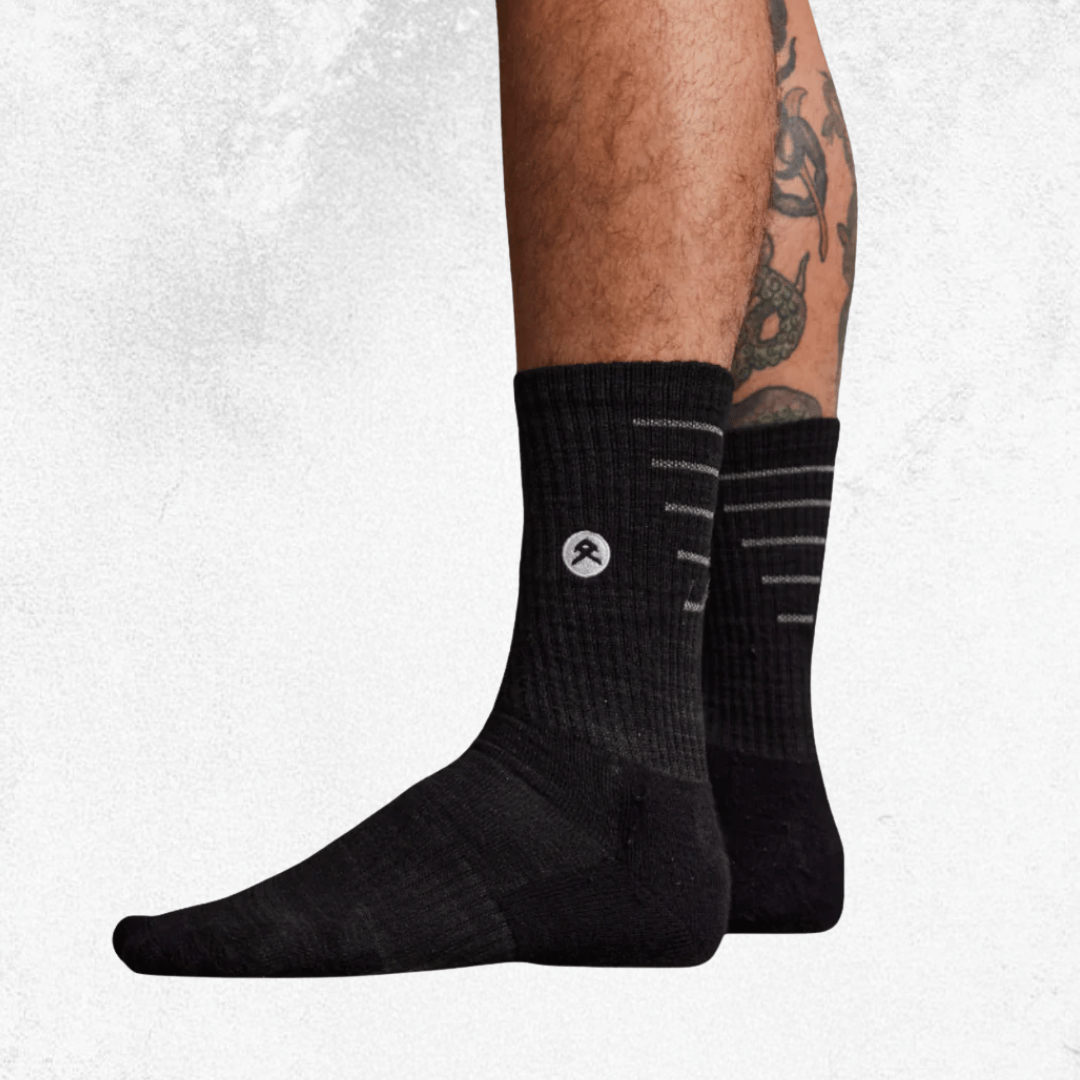 Black crew socks with a small white circular logo on the side, shown worn on a person's feet against a light textured background.