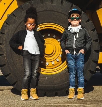 Two Kids standing next to truck wheel with glasses on. 