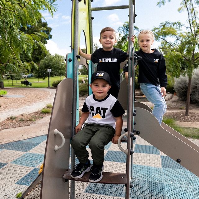 Clarico-Text Two images Kids wearing CAT Infant Ringer tee and sitting in a park on a seesaw and slide ladder