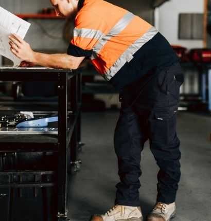 A man leaning over a work bench wearing Jet-Lite utility pants and a hi-vis shirt