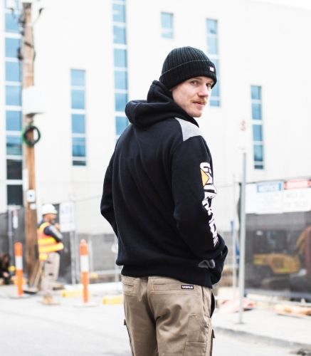 Man wearing the CAT Logo Panel Hooded Sweatshirt out front of construction site 