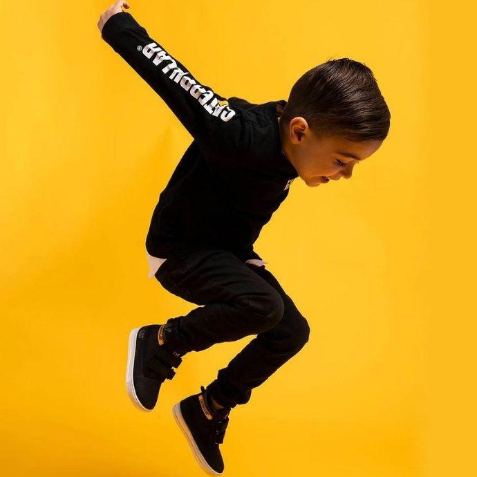 Kids Cat Workwear Trademark Banner Zip Sweatshirt | Man Cave Workwear A kid wearing CAT Kids Puffer Jacket and jumping