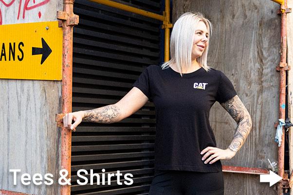 Women tradie with tattoos wearing CAT workwear Shirt outside near construction site.