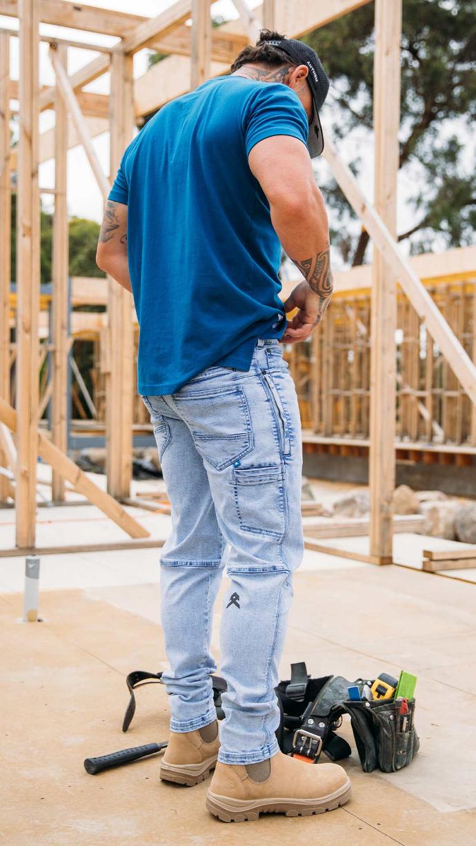 Tradie with tattoos wearing light blue Anthem Tech Stretch Denim Jeans on construction site.